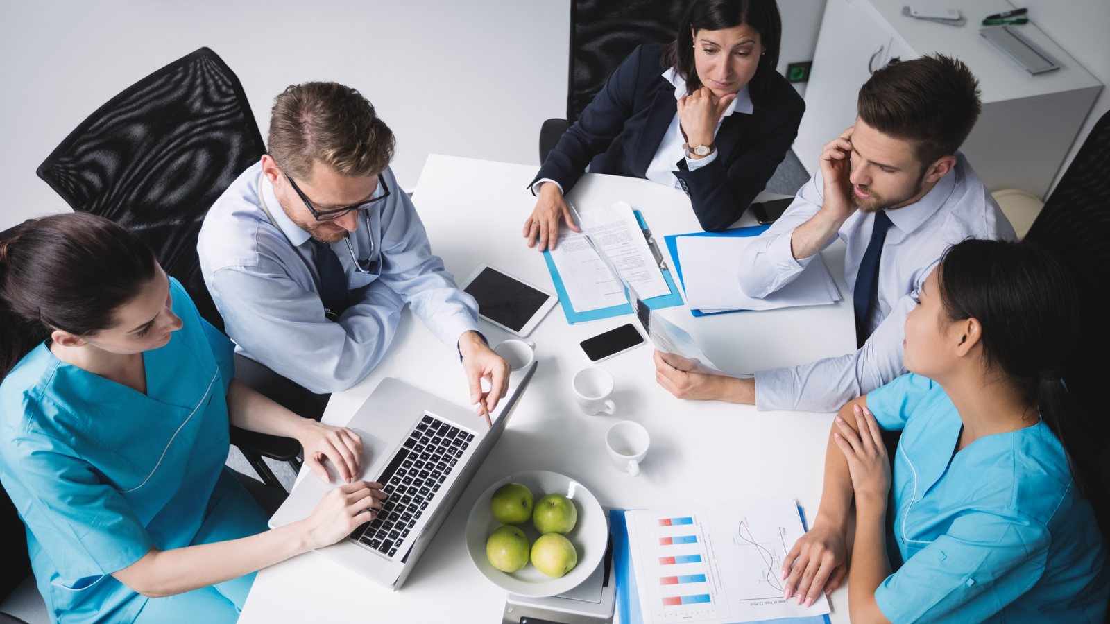 Medical practice leadership team reviewing performance reports and charts around a conference table